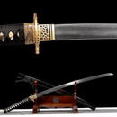 Close-up of an ornate katana hilt with gold details and black wrap, next to a displayed curved blade on a wooden stand. Tatsu Katana .