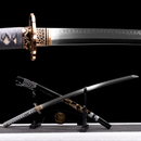A polished steel katana with a detailed guard on a stand, gray handle wrap, and ornate scabbard against a black backdrop. Nami Katana .