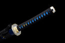 Close-up of a katana handle with black and blue wrap, gold accents, and decorative tsuba against a black background. Aoi Ryu Katana.