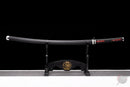 Black katana with red diamond-patterned handle on a stand with dragon emblem against a black background. Tanjiro Katana.