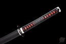 Close-up of a katana handle with black wrap and red details on a matte black scabbard, isolated on black background. Tanjiro Katana.