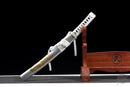Silver tanto with a white handle, gold dragon design, placed on a wooden stand against a black background. Ryūjin Tanto.